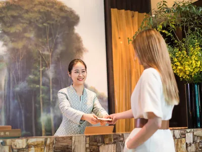 A hotel reception desk featuring a natural stone surface with a smiling receptionist interacting with a guest.