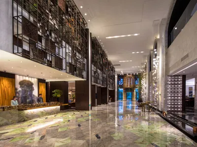 A modern hotel lobby with marble flooring, glass walls, and metallic accents.