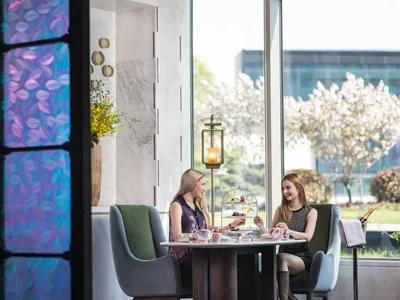 Two women enjoying a meal at a round table in a modern restaurant with glass walls and marble interior.