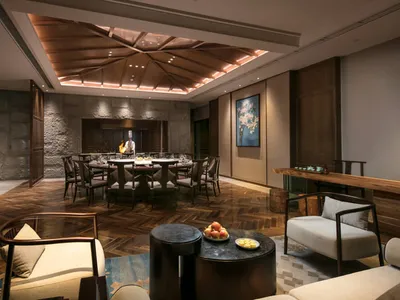 A cozy hospitality interior featuring wooden furniture and a stone wall with a round table and chairs in the center, illumina