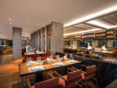 Modern restaurant interior with marble tables and chairs, stone flooring, and open kitchen counter.