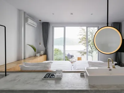 Modern minimalist hotel suite featuring a concrete floor, glass window overlooking the lake, and a circular light fixture.
