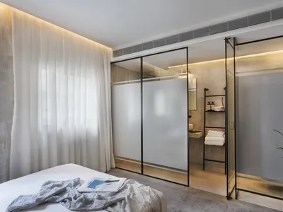 Modern minimalist bedroom with glass sliding doors, metal frames, and concrete floor.