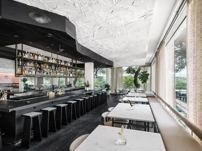 Modern cafe bar with white concrete precast walls and ceiling, featuring a well-lit bar area with stools and a long table for