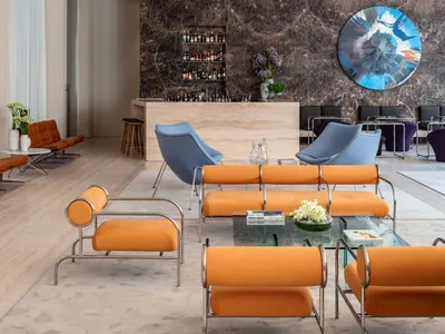 Modern hotel lobby featuring orange leather seating, marble accents, and metal framework.