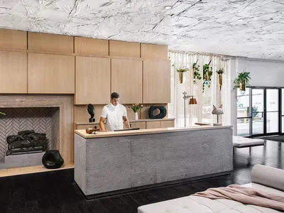 A modern, minimalist hotel reception desk made of concrete with a wooden cabinet and a cozy fireplace in the background.
