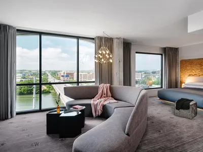 Modern hotel room featuring a contemporary couch, bed, and large window overlooking a cityscape.