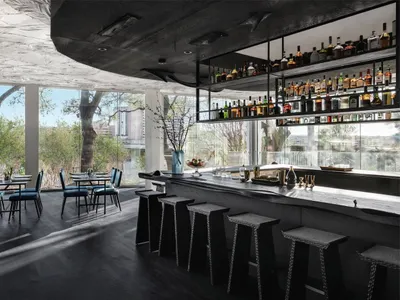 A modern restaurant bar interior with black wooden elements, seating for patrons, and a well-stocked bar.