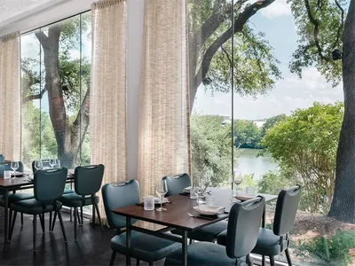 A modern restaurant interior featuring glass windows with a scenic view of trees and water.