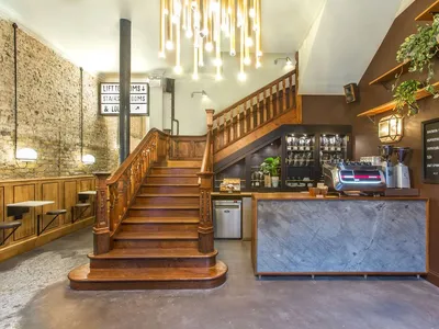 A cafe interior with wooden stairs, concrete flooring, and plants.