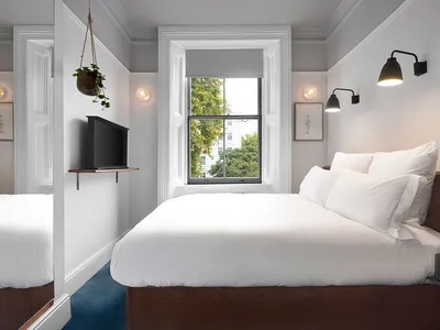 A minimalist bedroom featuring a white bed with a wooden headboard, white textiles, and minimalist decor.
