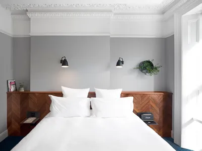 A minimalist bedroom with a white bed, wooden headboard, and black wall-mounted lamps.