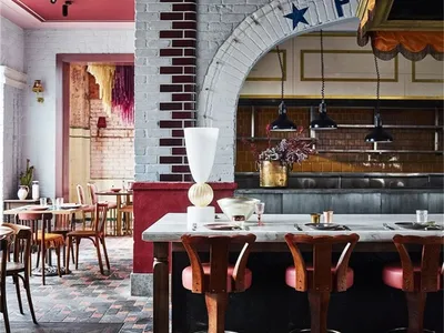 Industrial restaurant interior with brick and white-rendered walls, featuring a bar counter with stools, tables, and pendant