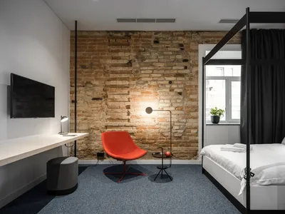 A minimalist bedroom featuring a red chair, a modern bed, and a brick wall.
