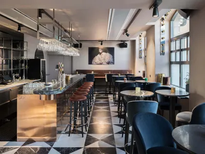 A modern bar area with a gold accent strip on the floor, marble countertops, and a row of high stools.