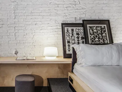 A modern minimalist bedroom featuring a wood frame bed with white bedding, a wooden nightstand with a round footstool, and fr