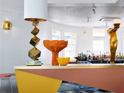 Modern restaurant bar featuring a brass counter, geometric lamp, and abstract sculptures.