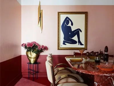 Modern restaurant dining room with a marble table, white chairs, and a gold vase with pink flowers.