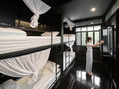 一間黑色室內的現代臥室，配有兩張鋪著白色織品的單人床，並以布簾提供隱私。