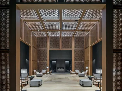 A modern hotel lobby featuring wooden materials and a high ceiling with intricate designs.