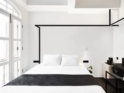 Modern minimalist bedroom with a single white bed featuring a black textile cover and metal headboard.