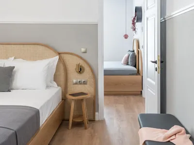 A minimalist bedroom featuring a wooden frame bed with white bedding and a wooden stool.