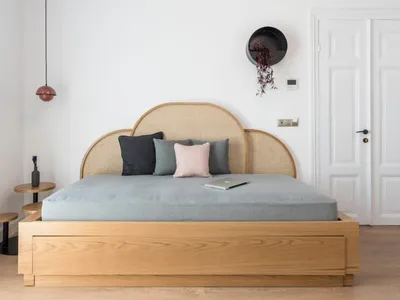 A modern bedroom with a light wood bed, featuring a woven headboard and colorful pillows.