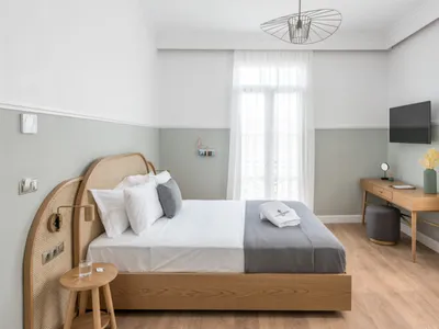 A modern, minimalist bedroom featuring a wooden frame bed with white bedding and grey accents, situated in a room with grey a