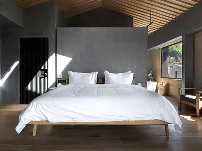 Modern minimalist bedroom featuring a wooden floor, white bedding, and large windows with skylights.