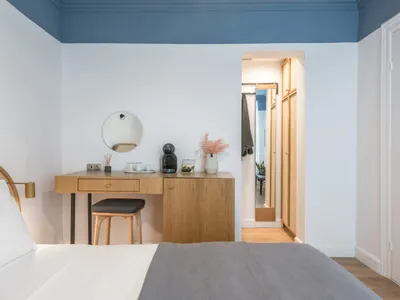A modern minimalist bedroom featuring a wooden vanity, rattan headboard, and a large bed with white bedding and a grey blanke