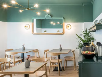A cozy breakfast cafe with wooden tables, green paint walls, and a modern chandelier.