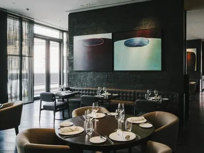 A restaurant interior with dark wood flooring and seating, glassware, and plates on tables, featuring industrial-style artwor