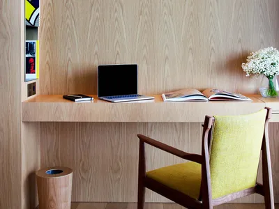 A minimalist home office workstation with a wooden desk, yellow upholstered chair, and light wood paneling.