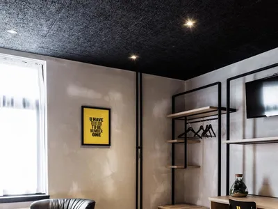 A minimalist hotel room with a black ceiling, white bedding, and a yellow motivational poster on the wall.