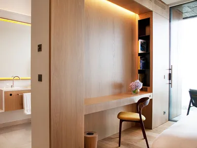 A minimalist hotel room featuring a wooden wall desk with a vases and books.