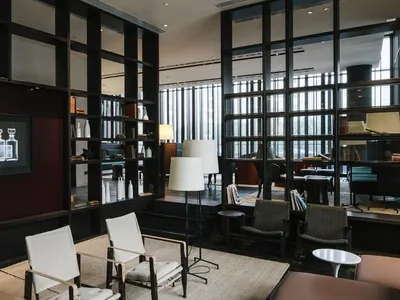 Modern hotel lobby with minimalist design featuring white chairs, floor lamps, and bookshelves.