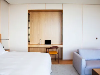 Modern minimalist bedroom featuring a wooden desk and white fabric furniture.