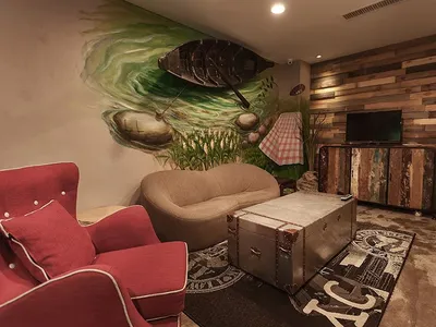 A cozy industrial-style living room with a retro trunk as a centerpiece, wooden panel walls, and a mural of a fishing boat on