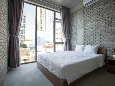 Modern minimalist bedroom with a bed, white bedding, grey curtains, and a brick wall