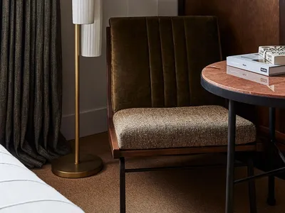 A modern bedroom with a fabric upholstered chair, wooden table, and marble top.