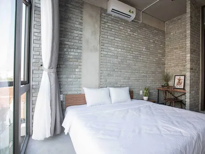 Modern bedroom with exposed brick walls, white bedding, and a large window
