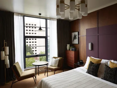 A modern hotel room featuring wooden paneling, fabric bedding, and metal accents.