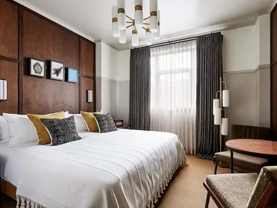 Modern hotel room featuring wooden walls, a white bed, and a metal table with chairs.