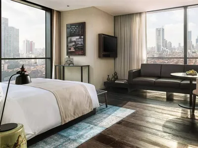 A modern hotel suite featuring a bed, sofa, and cityscape view.