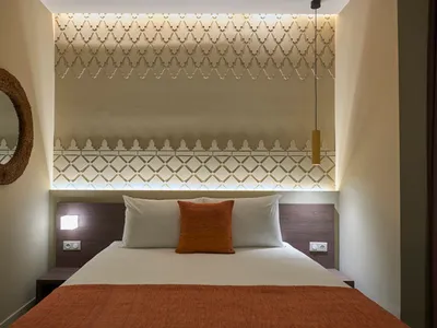 Modern bathroom with white and orange bedding on a bed, textured white walls, and a round mirror.