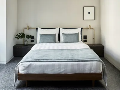Modern minimalist bedroom featuring a wooden bed frame with metal handles, white bedding, and dark grey accents.