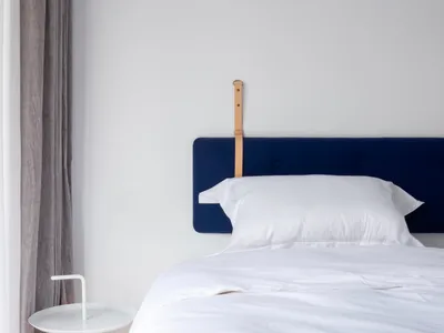 A minimalist bedroom featuring a blue upholstered bed with a white bedspread, white bedside table, and minimalist decor.
