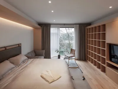 A minimalist bedroom featuring wood elements, a comfortable bed, and a large window.