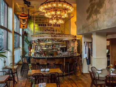 A modern restaurant with wooden tables, metal chairs, and a glass chandelier.