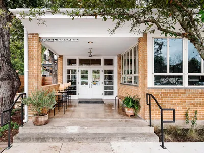The exterior of a cafe with white brick walls, concrete flooring, and potted plants on steps.